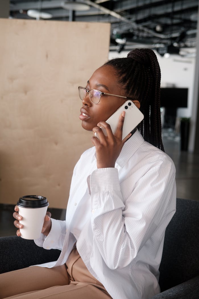 African American businesswoman speaking on phone while holding coffee in modern office.