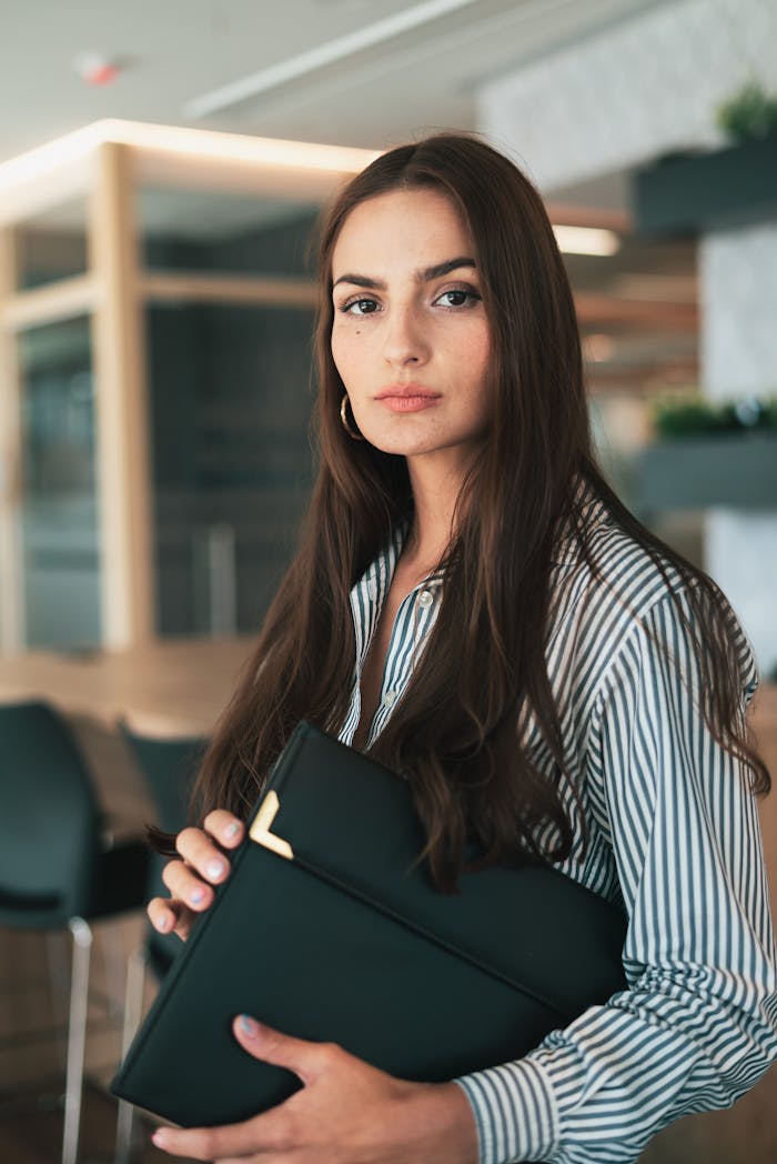 Portrait of a confident businesswoman with long hair holding documents in a modern office setting.